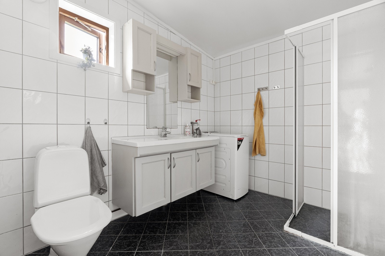 Badet er helflislagt og utstyrt med behagelig gulvvarme. Praktisk baderomsinnredning med underskap, samt opplegg for vaskemaskin. Nytt dusjkabinett vil bli satt inn før visning.