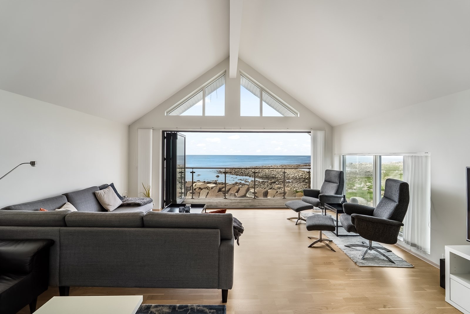 Stua har stor takhøyde og kan åpne balkongdørene som gir panoramautsik utover havet. Galleribilde