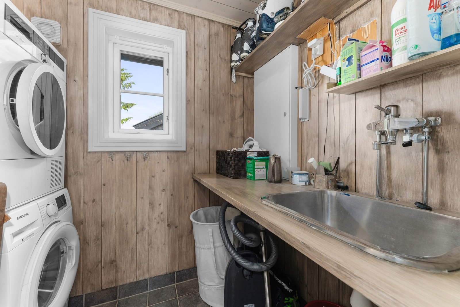 Et romslig og svært praktisk vaskerom med flislagt gulv og elektriske varmekabler. Vegger og himling er kledd med panel og tømmer. Rommet er utstyrt med utslagsvask, opplegg for vaskemaskin og elektrisk styrt ventilasjon. Galleribilde