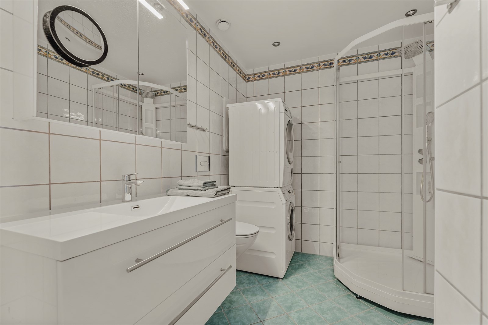 Praktisk flislagt bad med varme i gulv. Badet er innredet med servantskap med heldekkende servant, vegghengt toalett, dusjkabinett og opplegg for vaskemaskin. Galleribilde