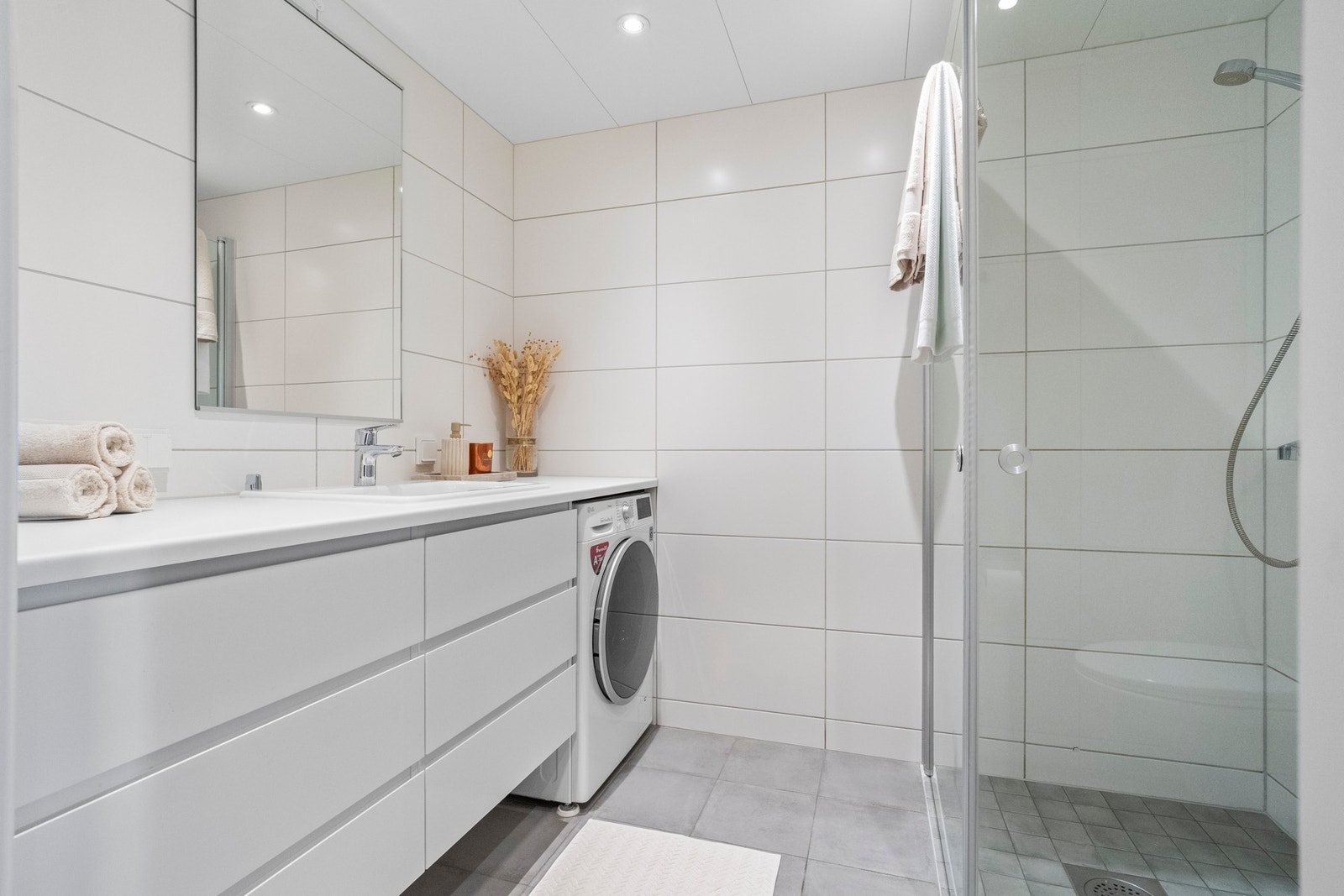 Badet har flislagte overflater og er utstyrt med varme i gulv, innfellbare dusjdører i glass og opplegg til vaskemaskin. Galleribilde
