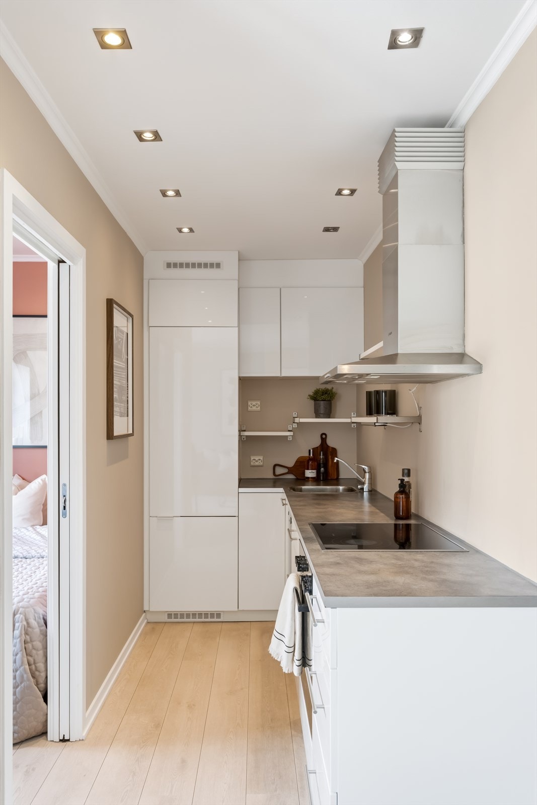 Kjøkkeninnredning med høyglansfolierte fronter, laminat benkeplate med nedfelt kum i rustfritt stål og ventilator med kullfilter. Galleribilde