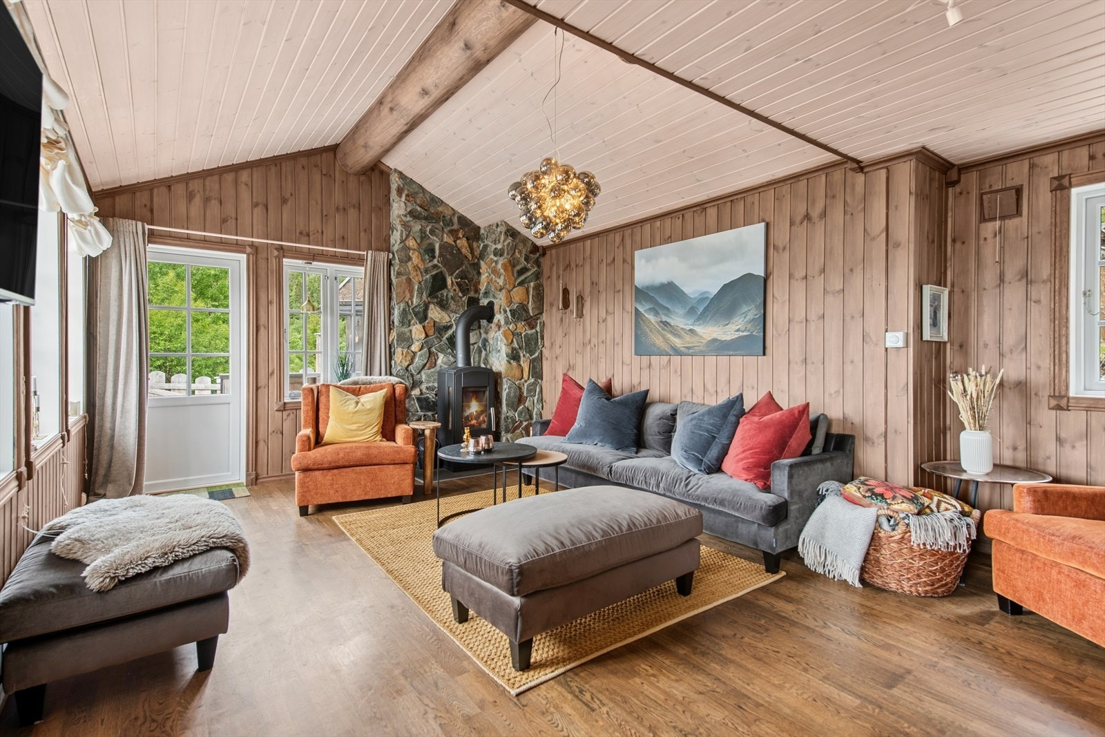 Luftig og innbydende stue med åpen himling, store vindusflater og herlig lysinnslipp fra flere himmelretninger. Rommet gir en varm og lun atmosfære med vedfyring som naturlig samlingspunkt. Galleribilde