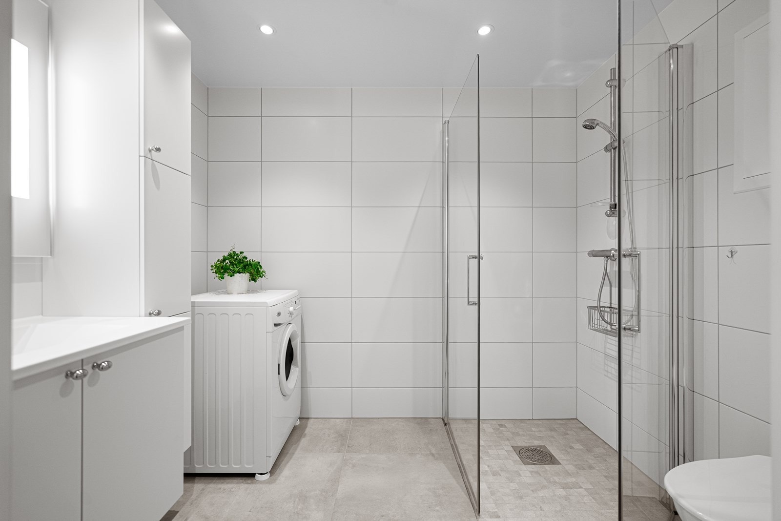 Flott, flislagt bad med moderne innredning, glass dusjvegger, vegghengt toalett og opplegg for vaskemaskin. Galleribilde
