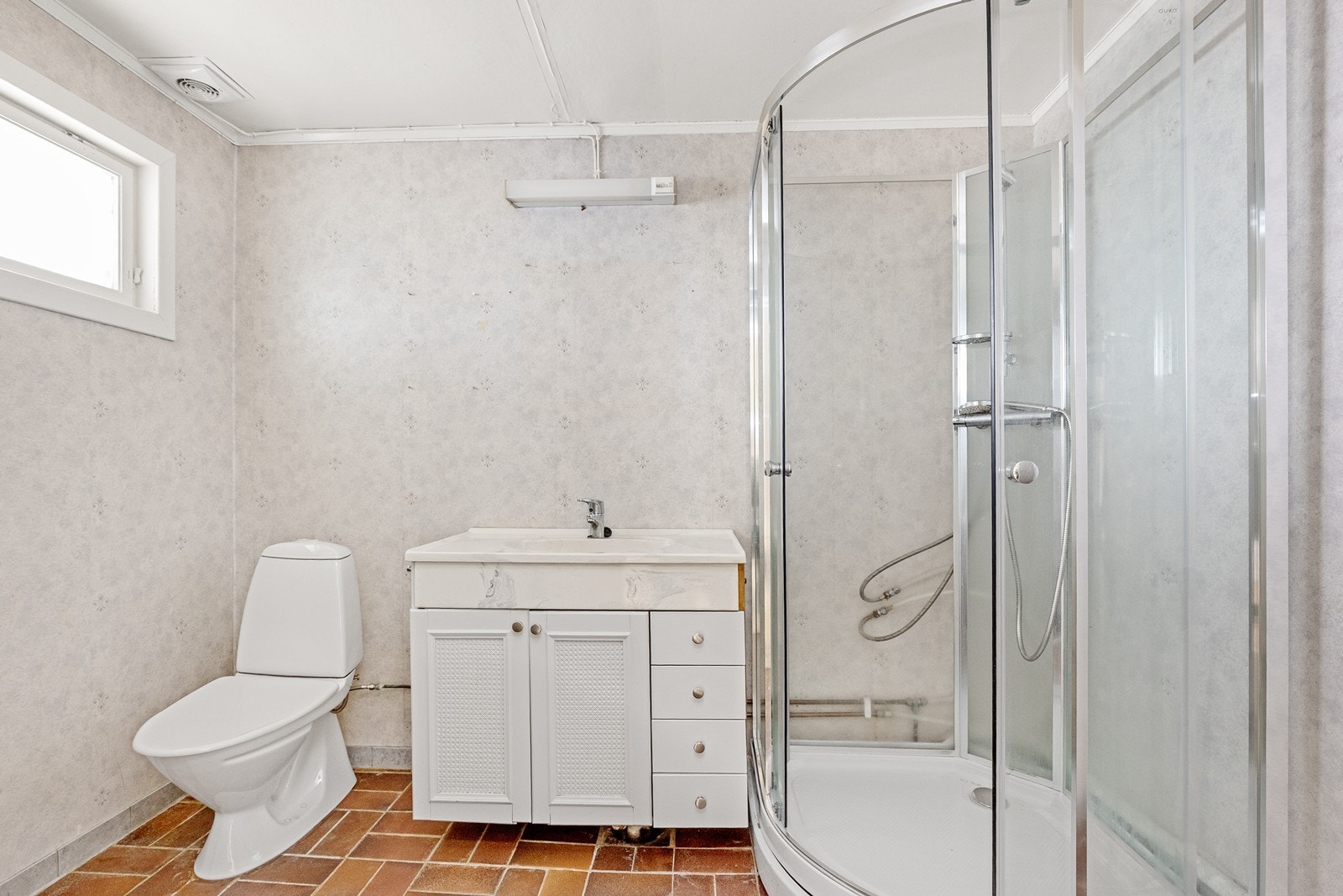 Badet i 1. etasje har flislagt gulv, våtromstapet og malte himlingsplater, samt elektrisk avtrekksvifte og dusjkabinett. Galleribilde