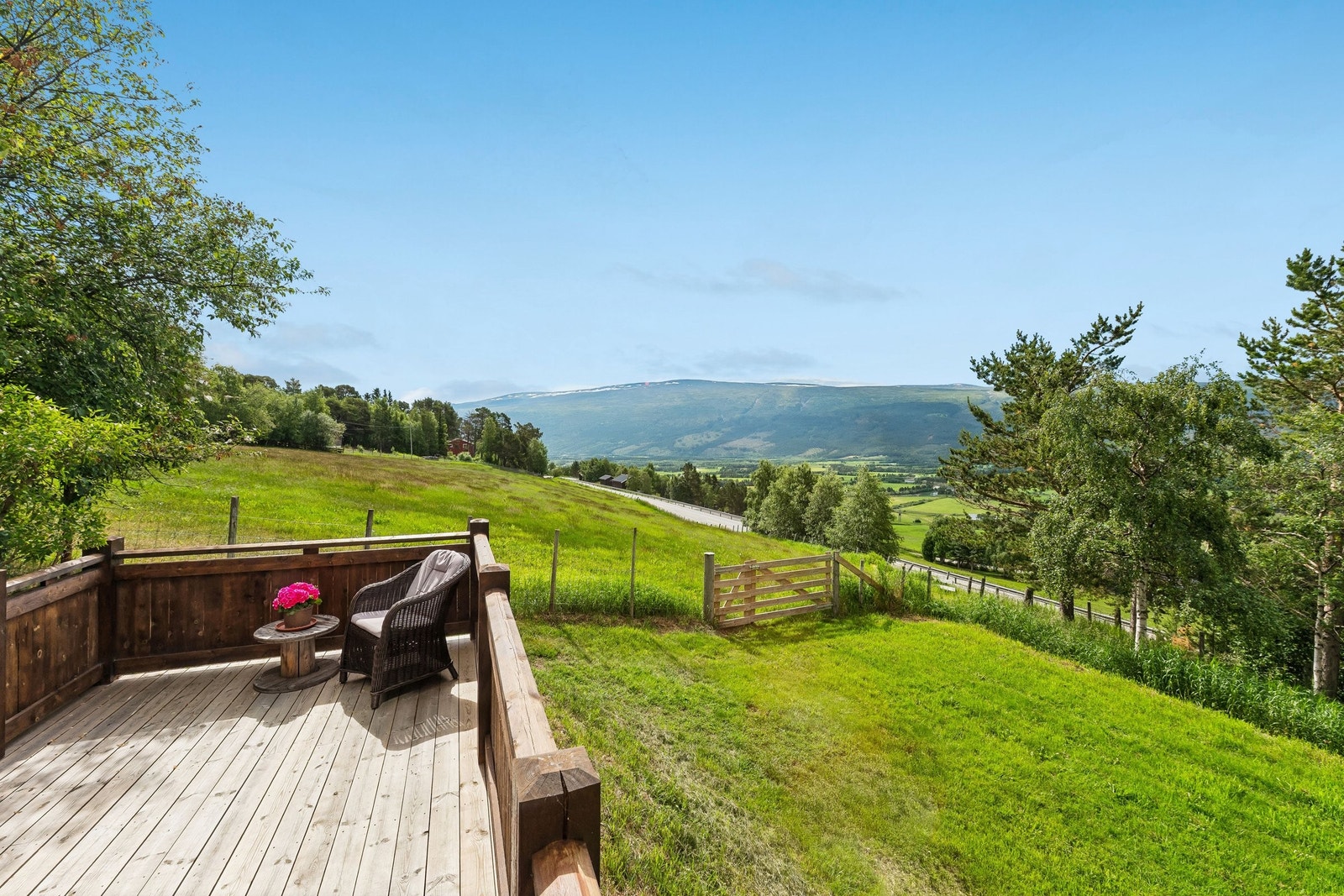 Utsikt fra terrasse på østsiden i 1.etg. Utsyn over opparbeidet plen på inngjerdet område og noe av den dyrka innmarka som hører til eiendommen. Sol fra morgen og utover dagen. Terrassen er forsterket for å tåle vekt av jacuzzi. Galleribilde