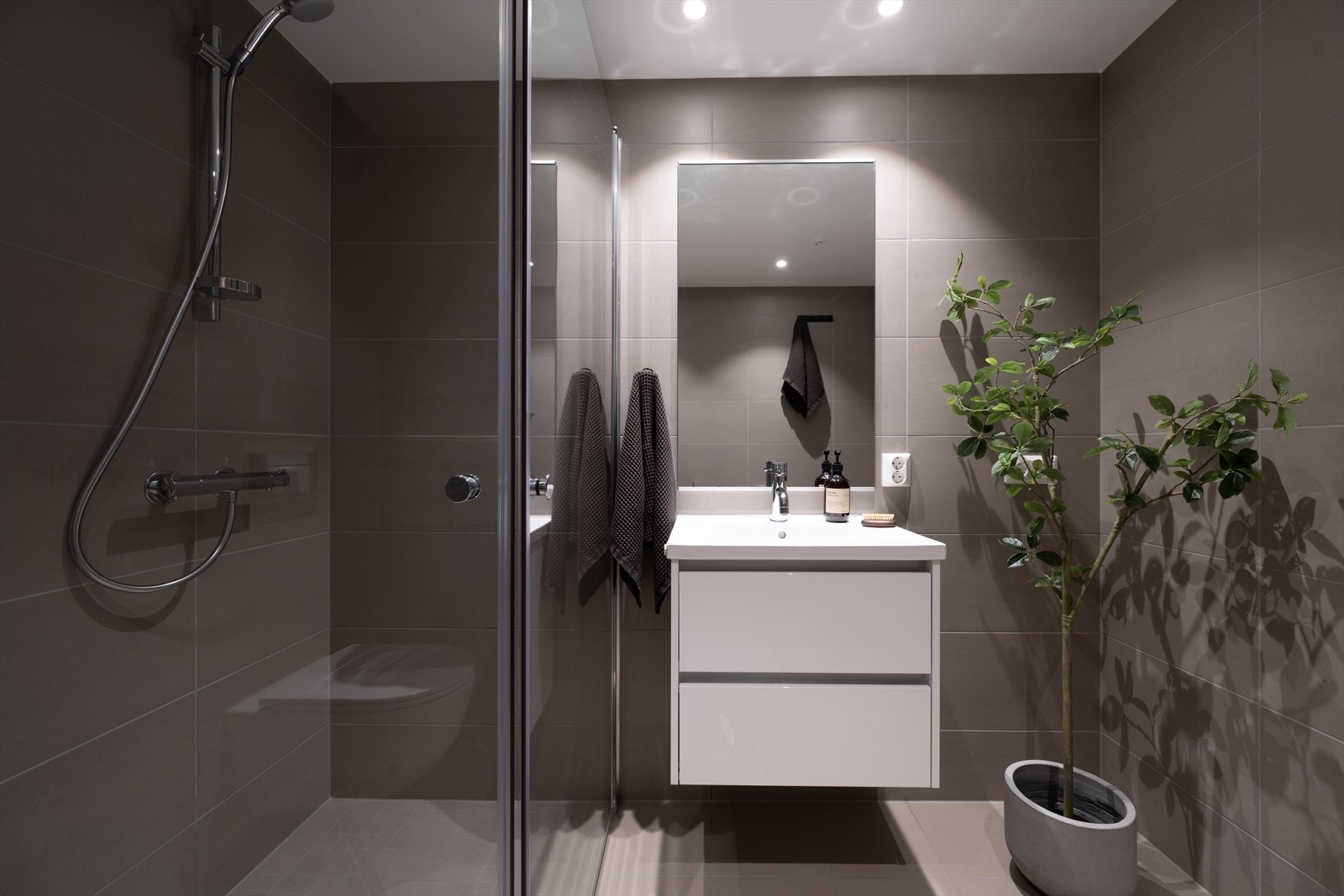 Badet er innredet med heldekkende servant, speil med belysning, veggmontert toalett og innfellbare dusjvegger/hjørnet. Galleribilde
