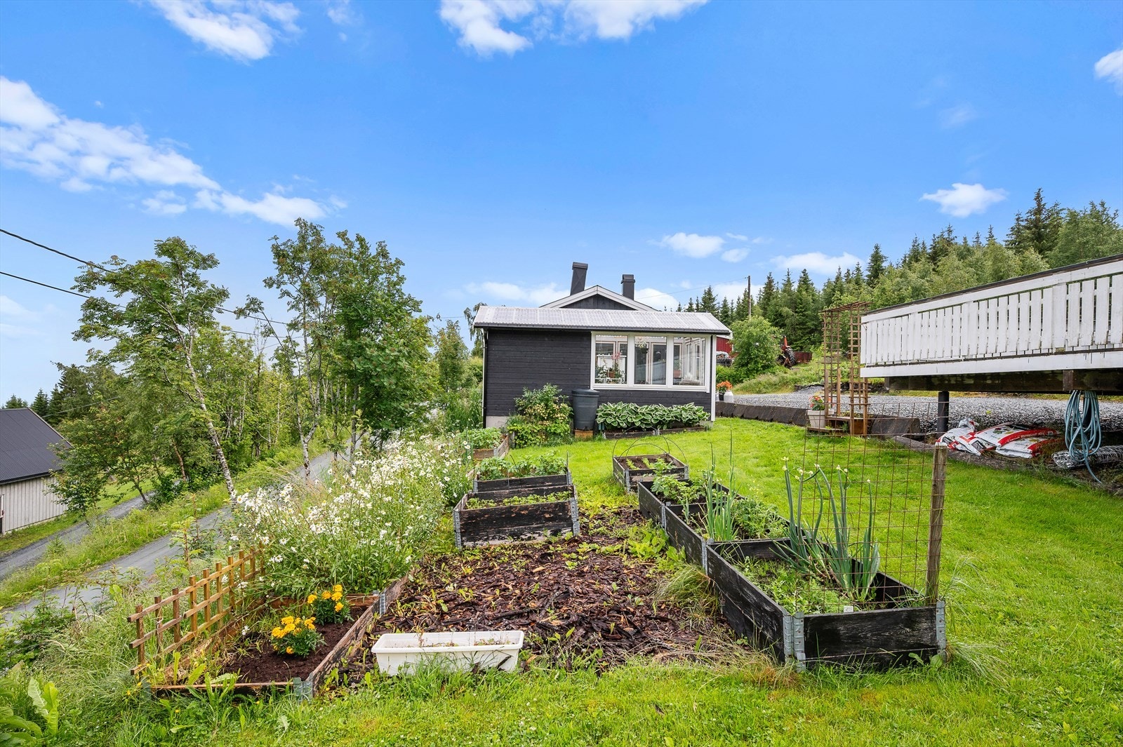 Eiendommen omfatter bl.a. en stor garasje, gapahuk og et drivhus, alle utført i en gjennomgående stil. Galleribilde