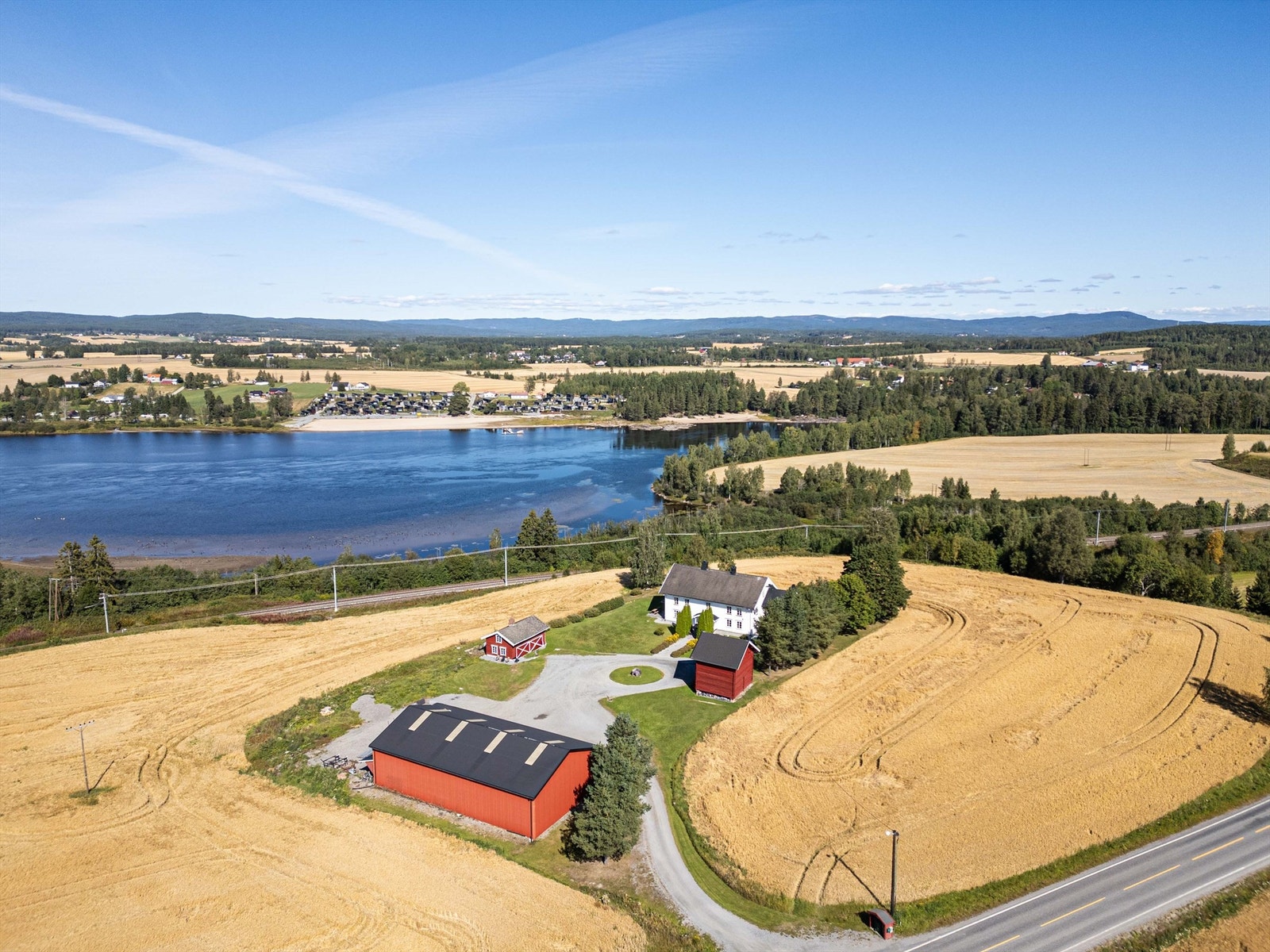 Sommerlig oversikt over eiendommen med omkringliggende jorder og vann. Galleribilde
