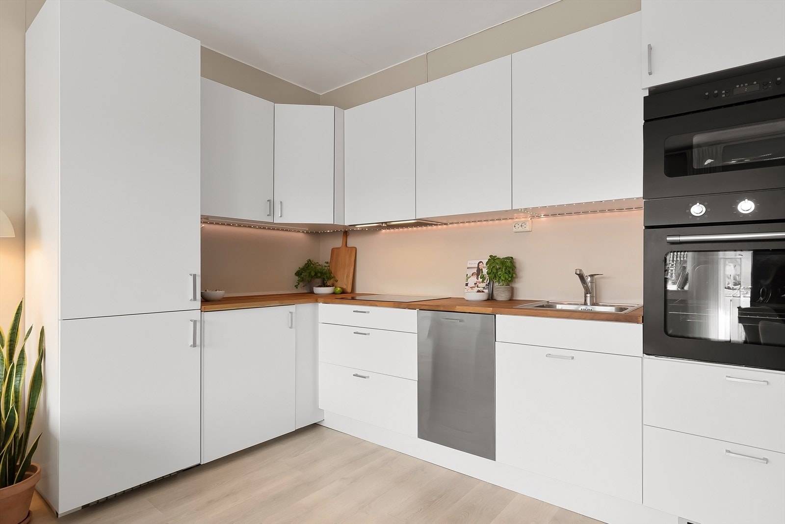 Stilrent kjøkken bestående av hvite, glatte fronter og benkeplate av heltre med nedfelt vask. Galleribilde