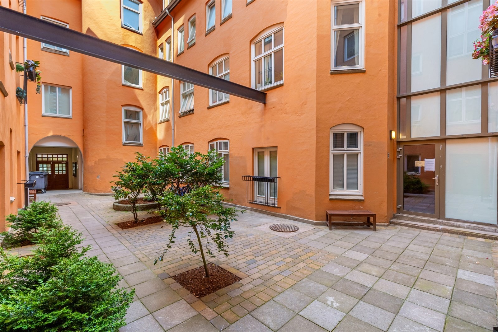 Det er en koselig stenbelagt bakgård med blomsterbed, sykkelstativ og diverse møbler. Galleribilde