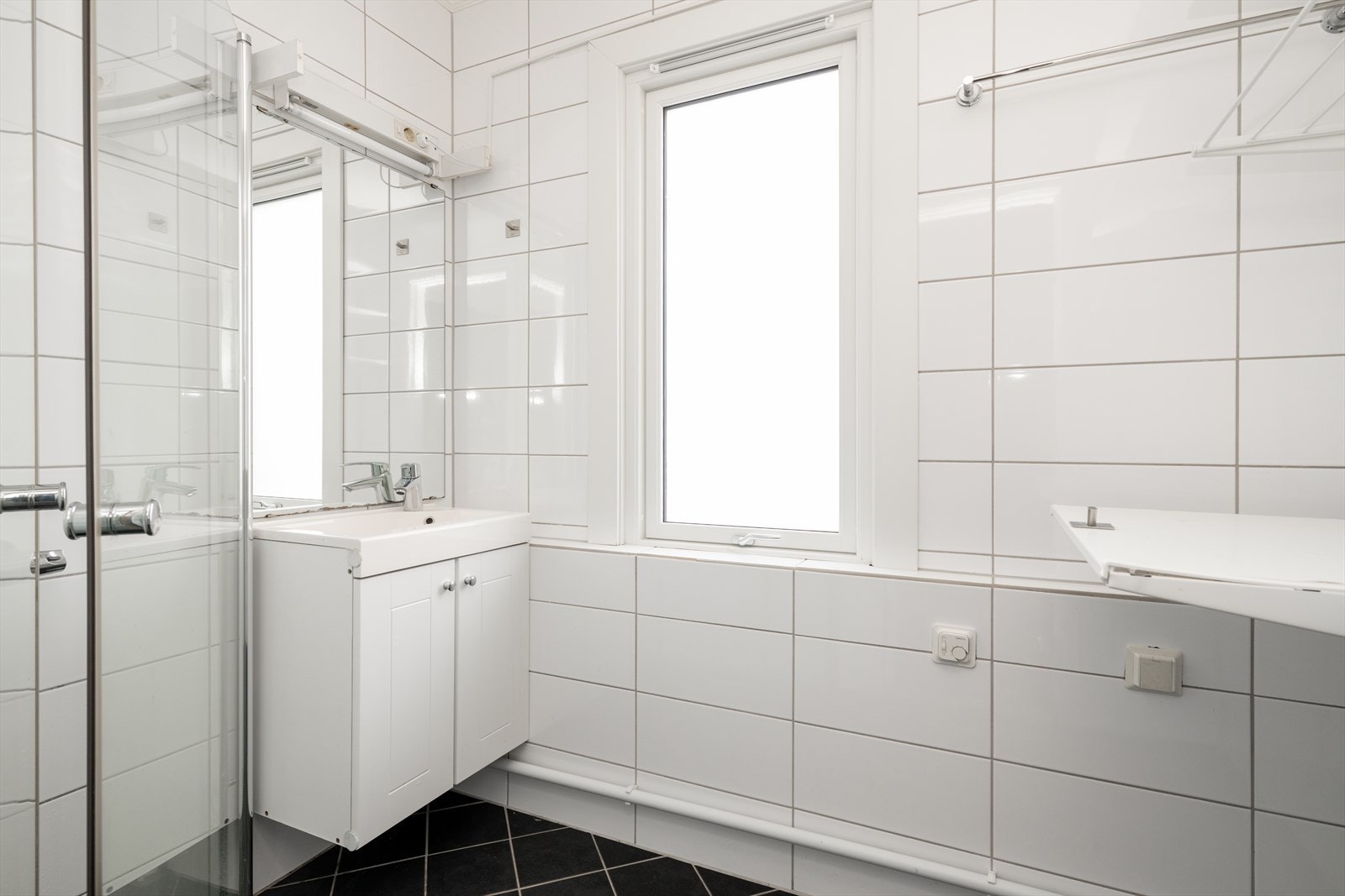 Flislagt bad med varmekabler, utstyrt med dusjvegger i glass, servantskap og opplegg for vaskemaskin. Galleribilde