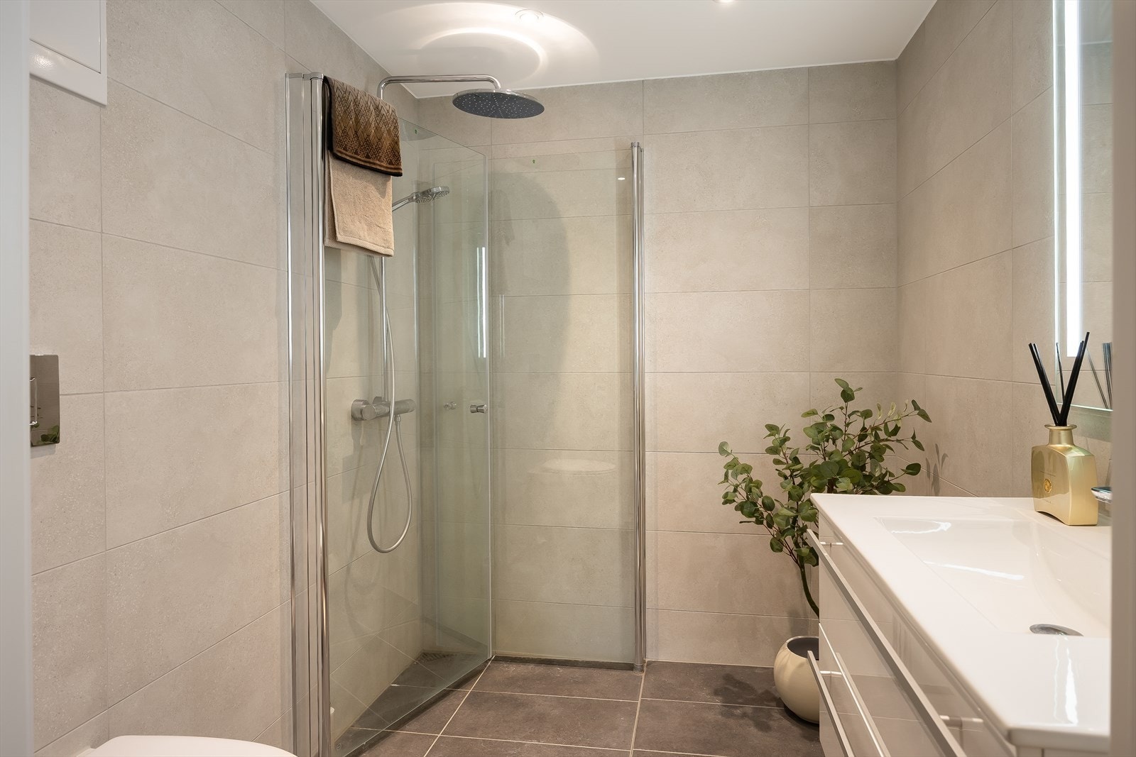 Badet har fliser å vegger og gulv, servant med underskap, speil med lys, vegghengt wc og dusjhjørne. Galleribilde