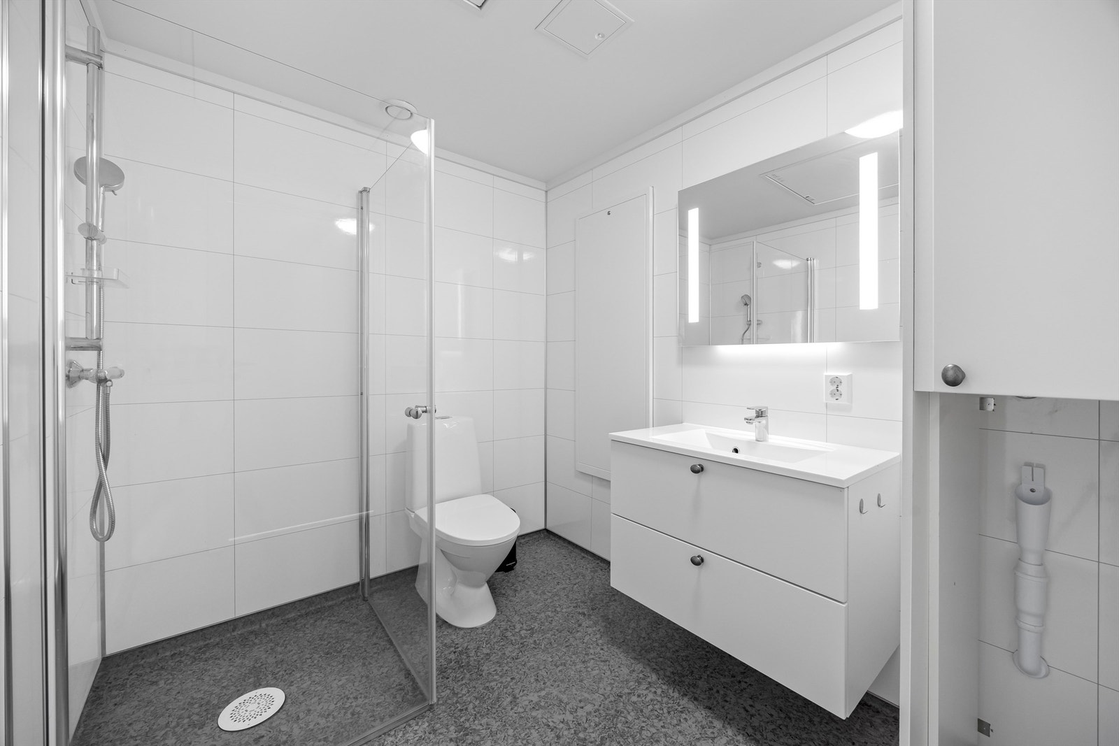 Lyst og pent baderom med opplegg til vaskemaskin, dusjhjørne, servant og toalett. Galleribilde