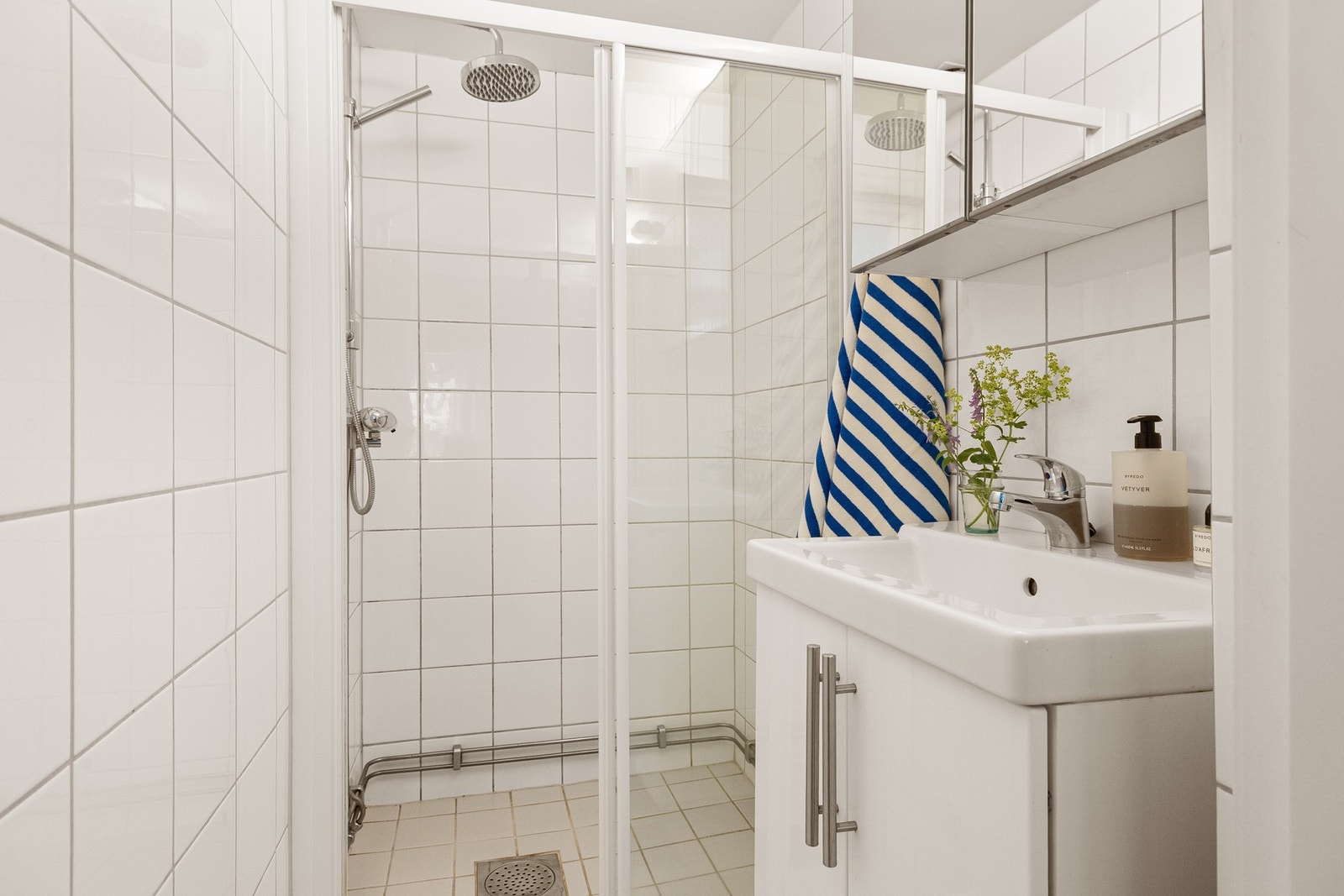 Det er pent flislagt, nedfelt servant med underskap, dusj med glassvegger og praktisk speilskap. Galleribilde