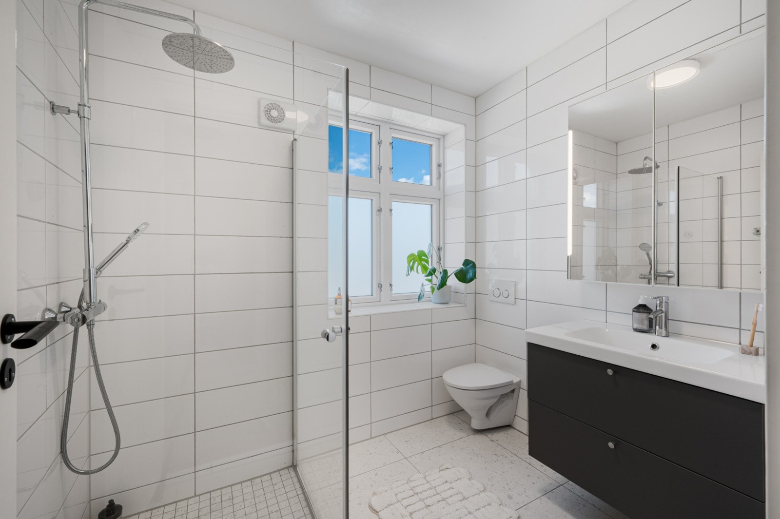 Badet er innredet med vegghengt toalett, dusjhjørne glassvegger, og baderomsmøblement med speil og belysning. Galleribilde