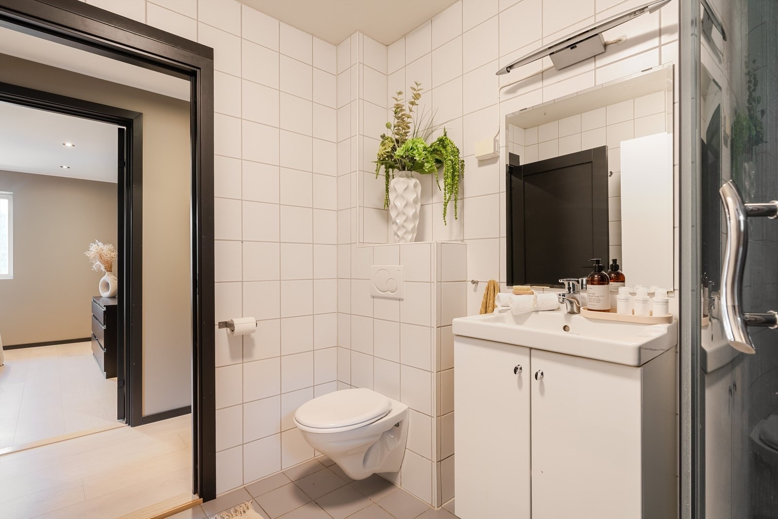 Med flislagte overflater og en funksjonell innredning med dusjkabinett, vegghengt toalett og servant med speil, fremstår badet praktisk og lettstelt. Galleribilde
