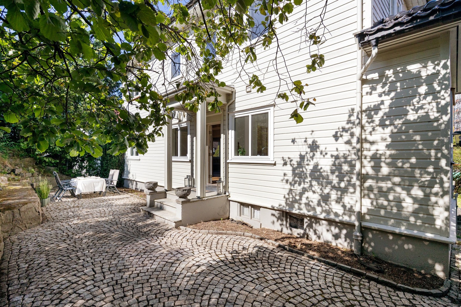 Sjarmerende brosteinsbelagt gårdsplass og et hyggelig inngangsparti omgitt av frodig beplantning. Galleribilde