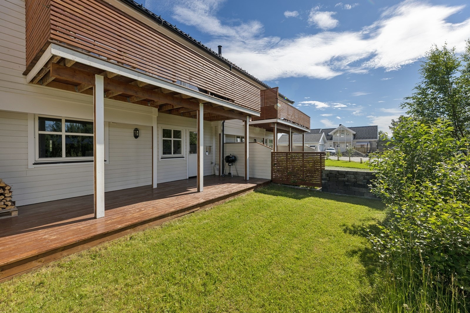 En stor delvis overbygd terrasse på bakkeplan, med videre tilkomst til hage med gressplen. Galleribilde
