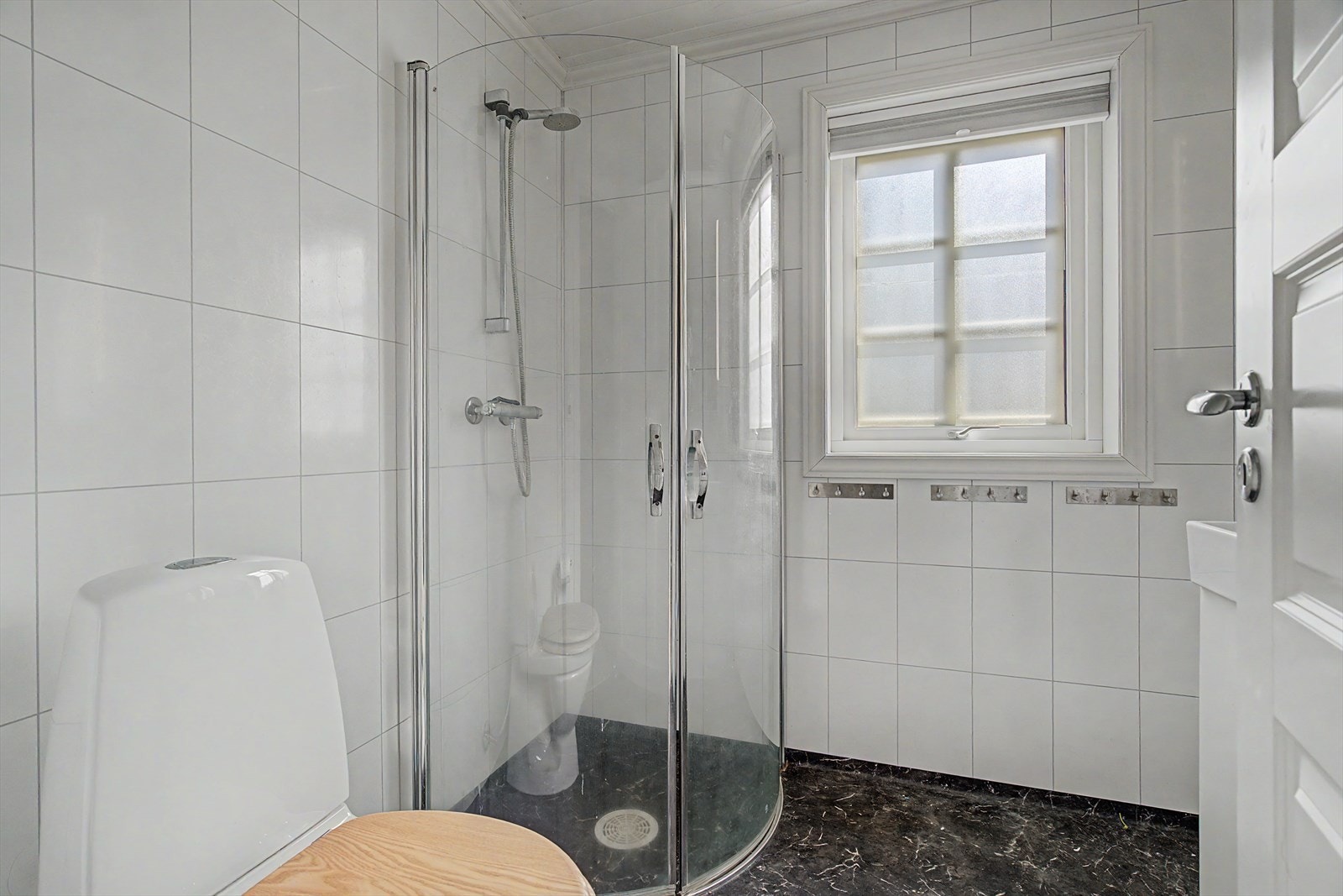 Badet er utstyrt med dusjhjørne, toalett og servantskap. Rommet har baderomsplater på veggene. Galleribilde