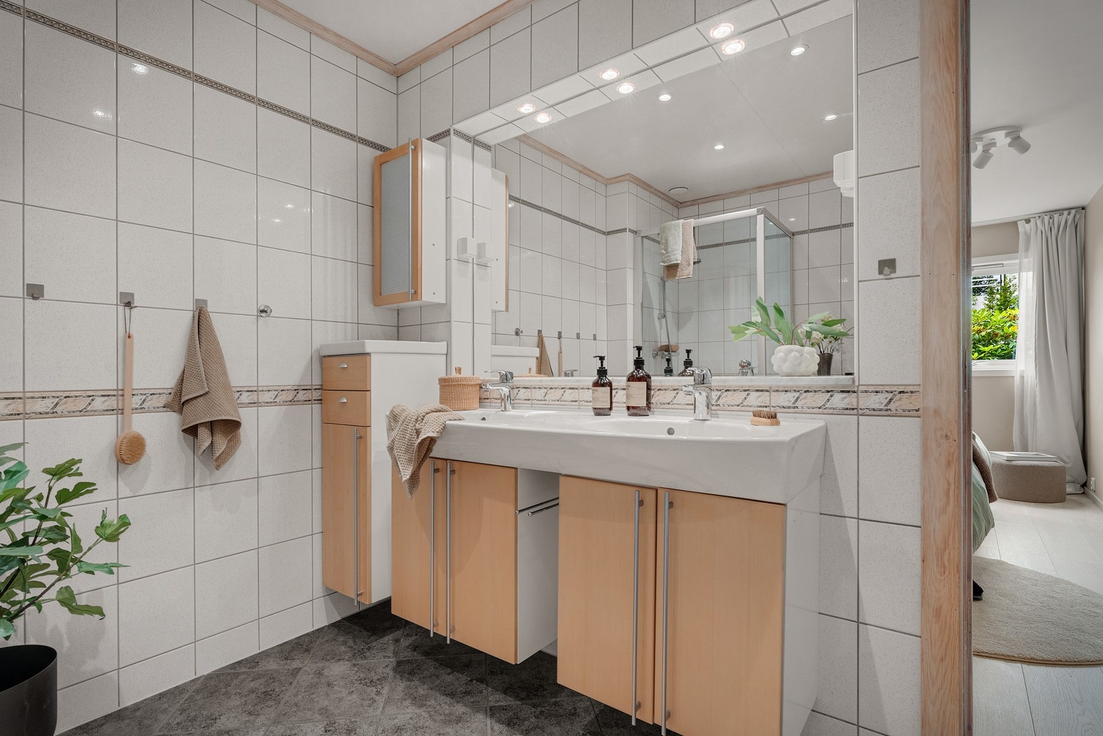 Helfliset baderom fra byggeår. Det er platekledd himling med innfelte downlights. Rommet inneholder opphevet dusjsone med dusjvegger, vegghengt servant med dobbel vask og skap, vegghengt toalett med innebygget sisterne og diverse skapplass/lagringssplass Galleribilde