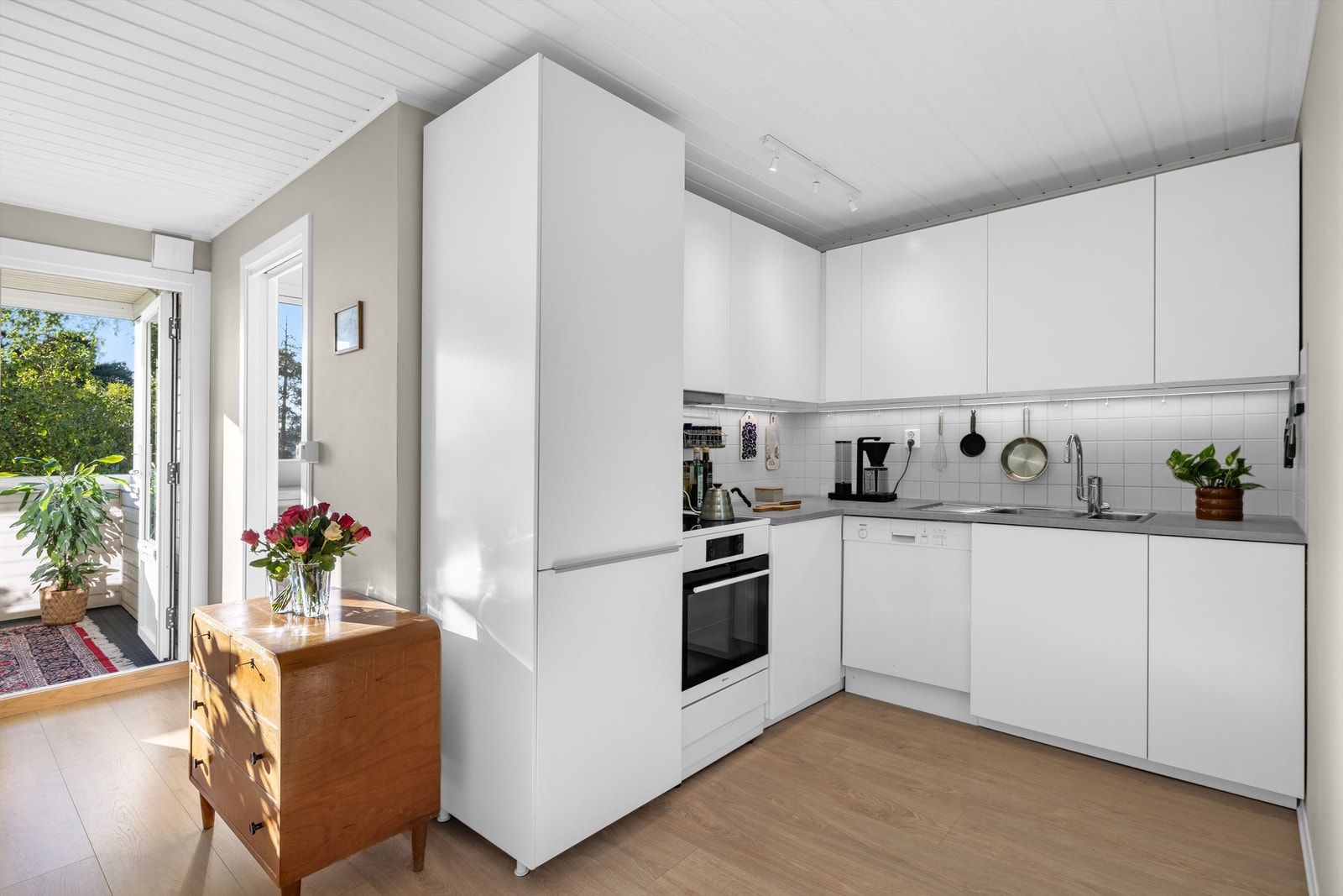 Innredning med glatte, hvite fronter, benkeplate med laminert overflate og nedfelt kjøkkenvask med armatur. Kjøkkenet har videre integrert kjøleskap med fryser, samt frittstående komfyr og oppvaskmaskin Galleribilde