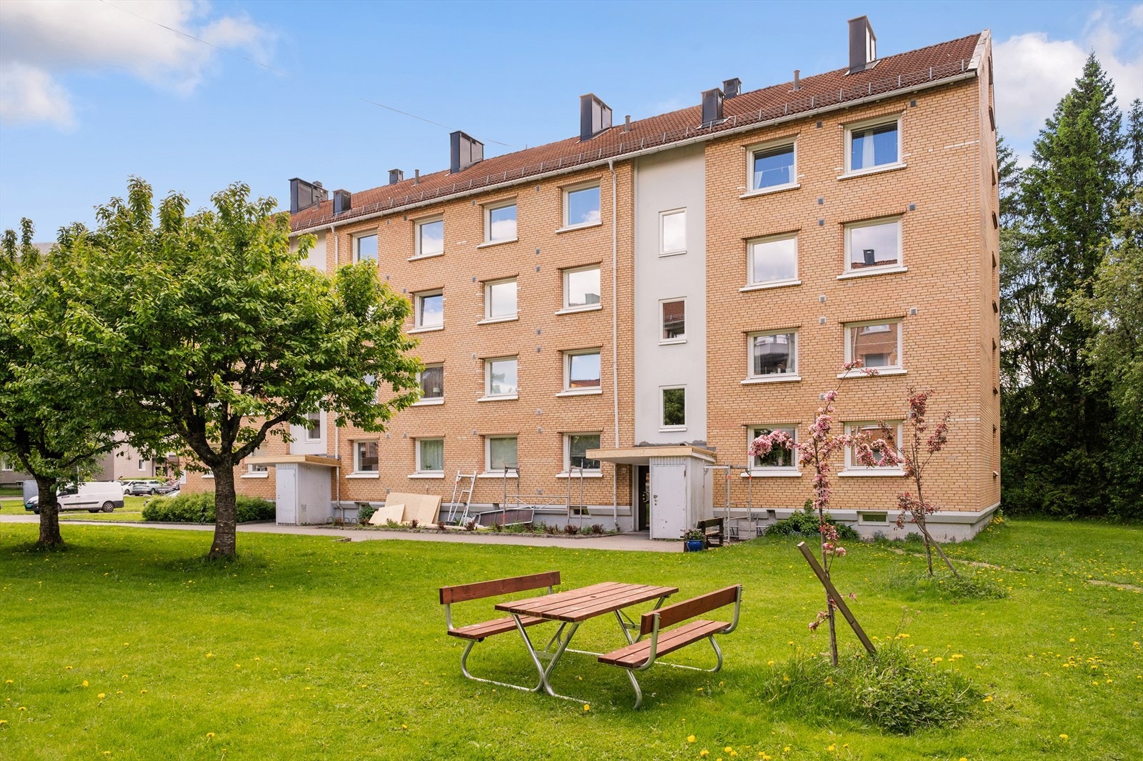 Stor felles tomt, opparbeidet med asfalterte adkomstveier/plasser, gressplen, beplantning, trær, lekeapparater, parkeringsarealer m.m. Galleribilde
