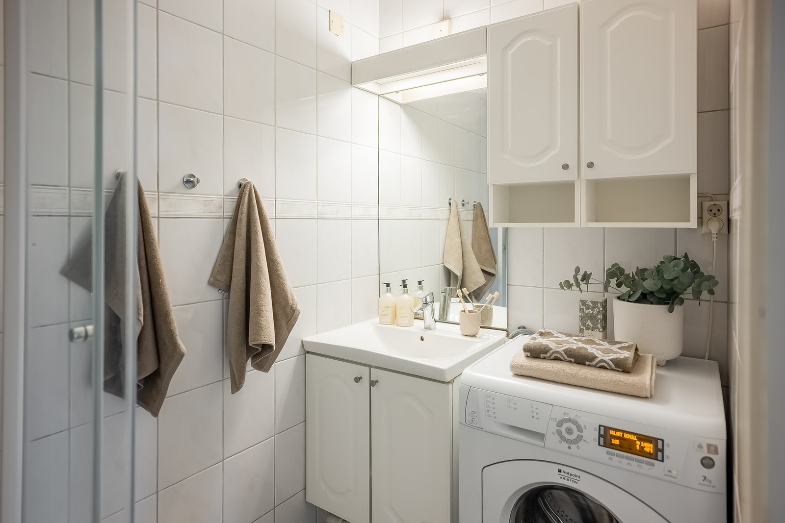 Pent flislagt bad med opplegg for vaskemaskin og dusjkabinett som minimerer eksponering av vann på det flislagte gulvet. Galleribilde