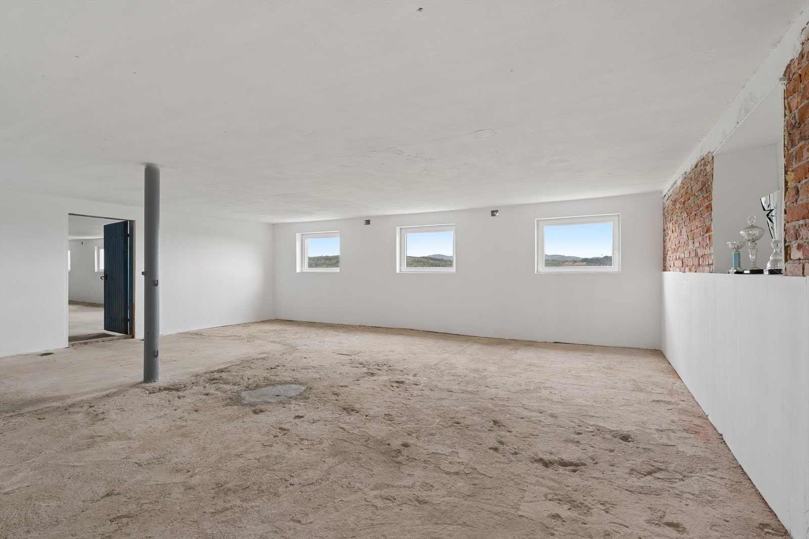 Stort, uinnredet rom i låven med betonggulv og synlig teglstein. Galleribilde