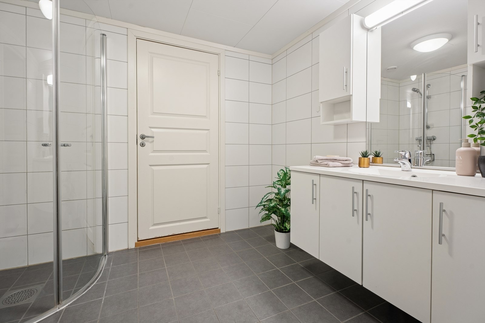 Badet er helfliset og innredet med en bred servant med underskap, speil med belysning og dusjvegger. Galleribilde
