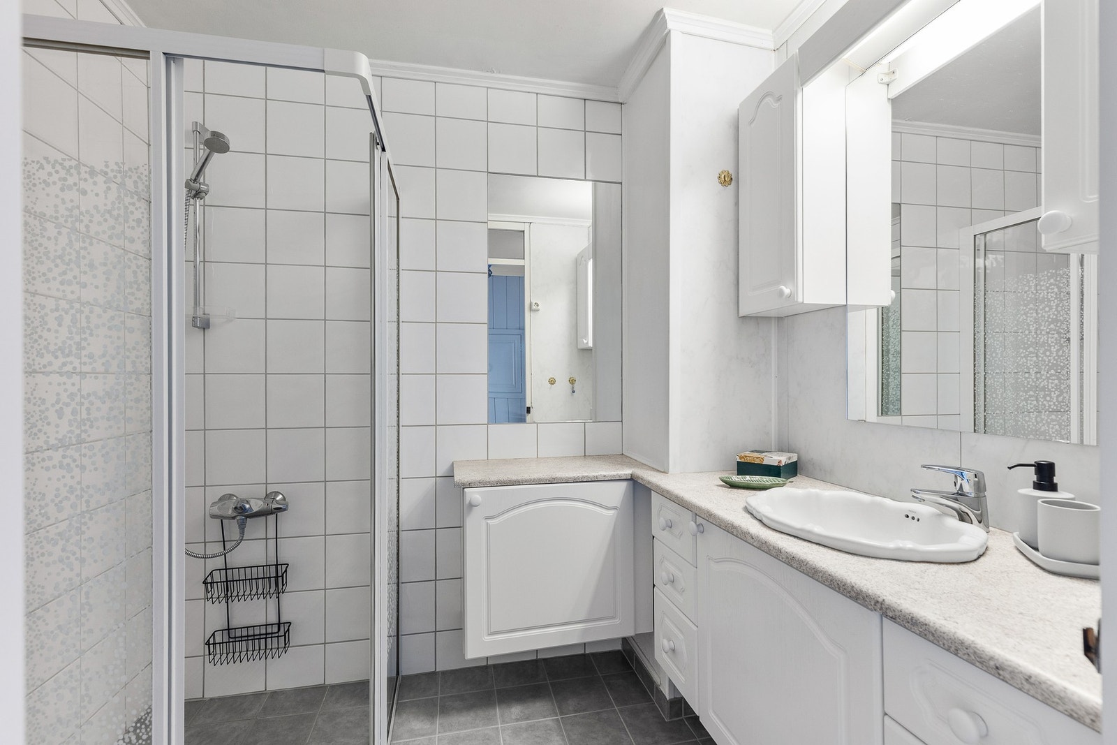 Flislagt baderom med speil med integrert belysning og servantskap med god oppbevaringsplass for hygieneartikler. Galleribilde
