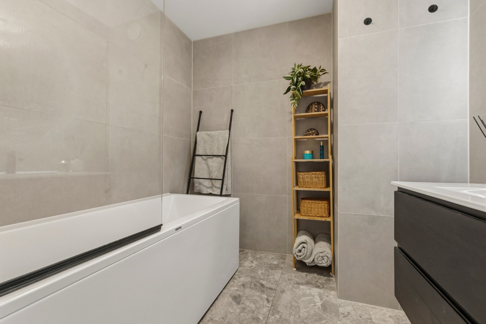 Det stilrene badet har store, lyse fliser og er innredet med badekar og moderne baderomsinnredning Galleribilde