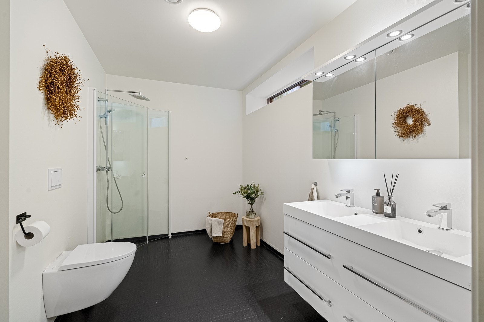 Badet er innredet med dobbel servant nedfelt i skuffeseksjon, speil med oppbevaring og vegghengt toalett. Dusjen har innfellbare dører som gir en fleksibel og plassbesparende løsning. Galleribilde