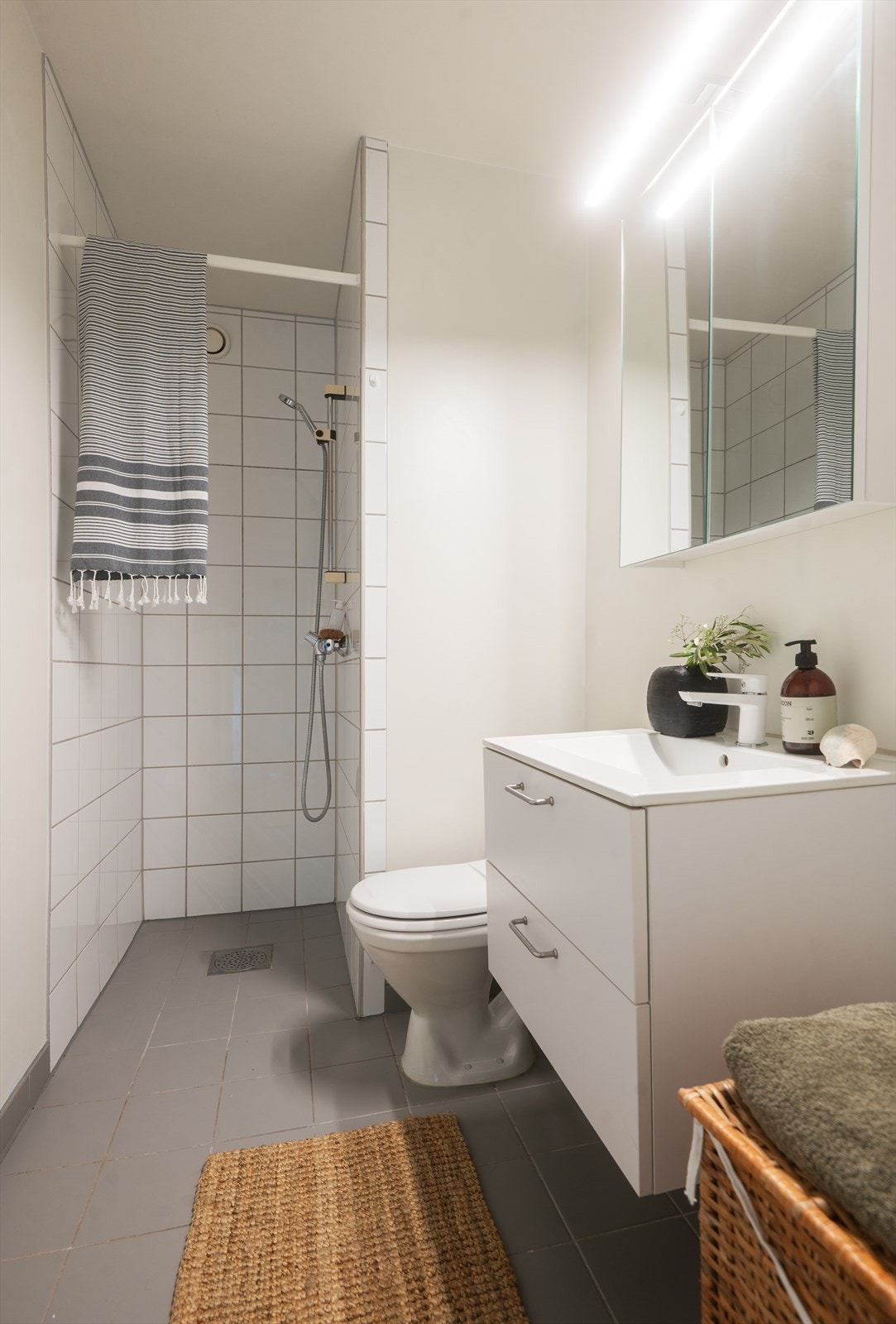 Pent og funksjonelt bad med flislagt gulvvarme og opplegg for vaskemaskin. Badet er innredet med nedfelt servant med underskap, speilskap, toalett og dusjhjørne med forheng. Galleribilde