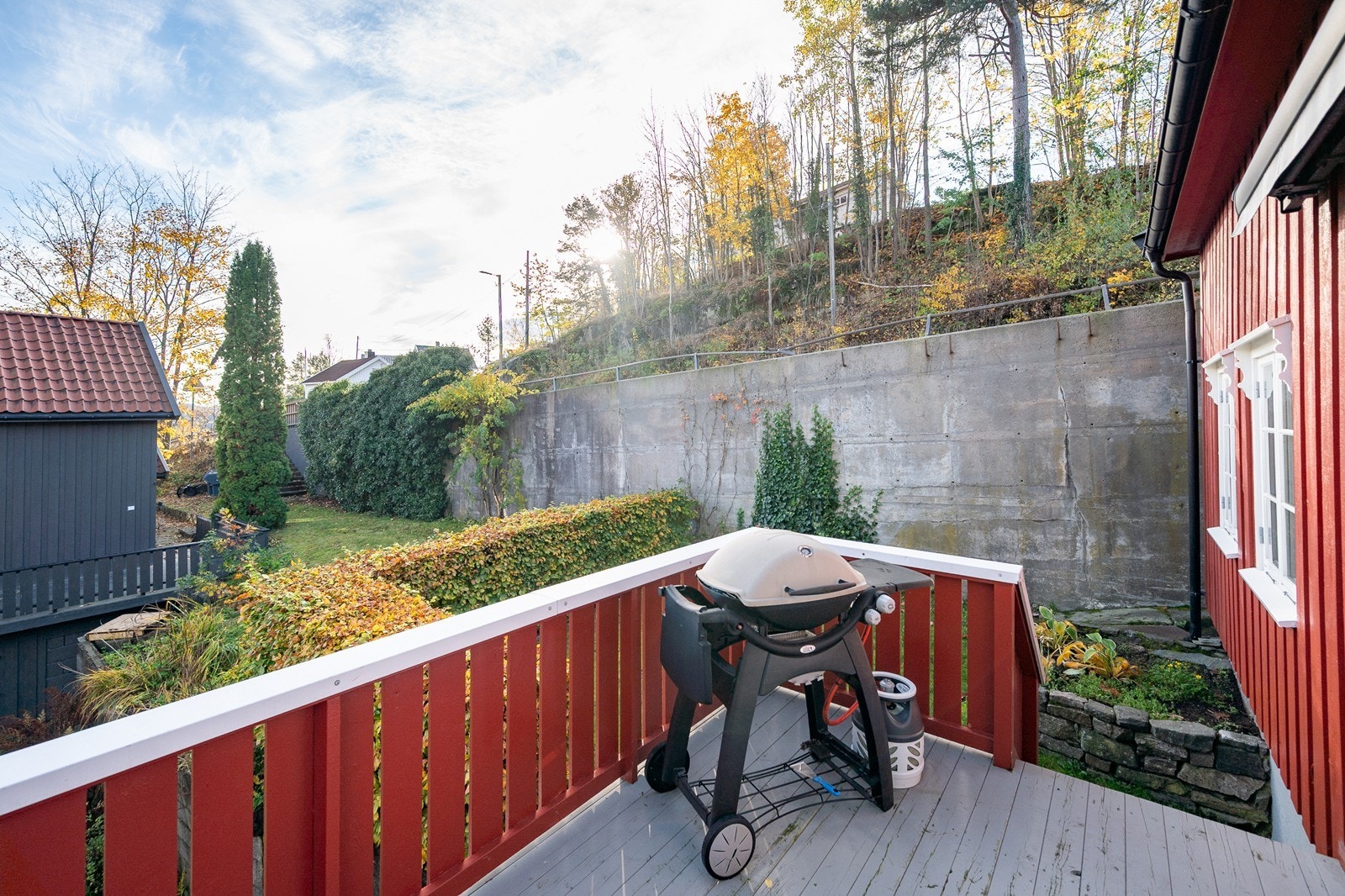 Terrasseområdet er delvis innrammet av vegetasjon og mur, med plass til utemøbler. Galleribilde