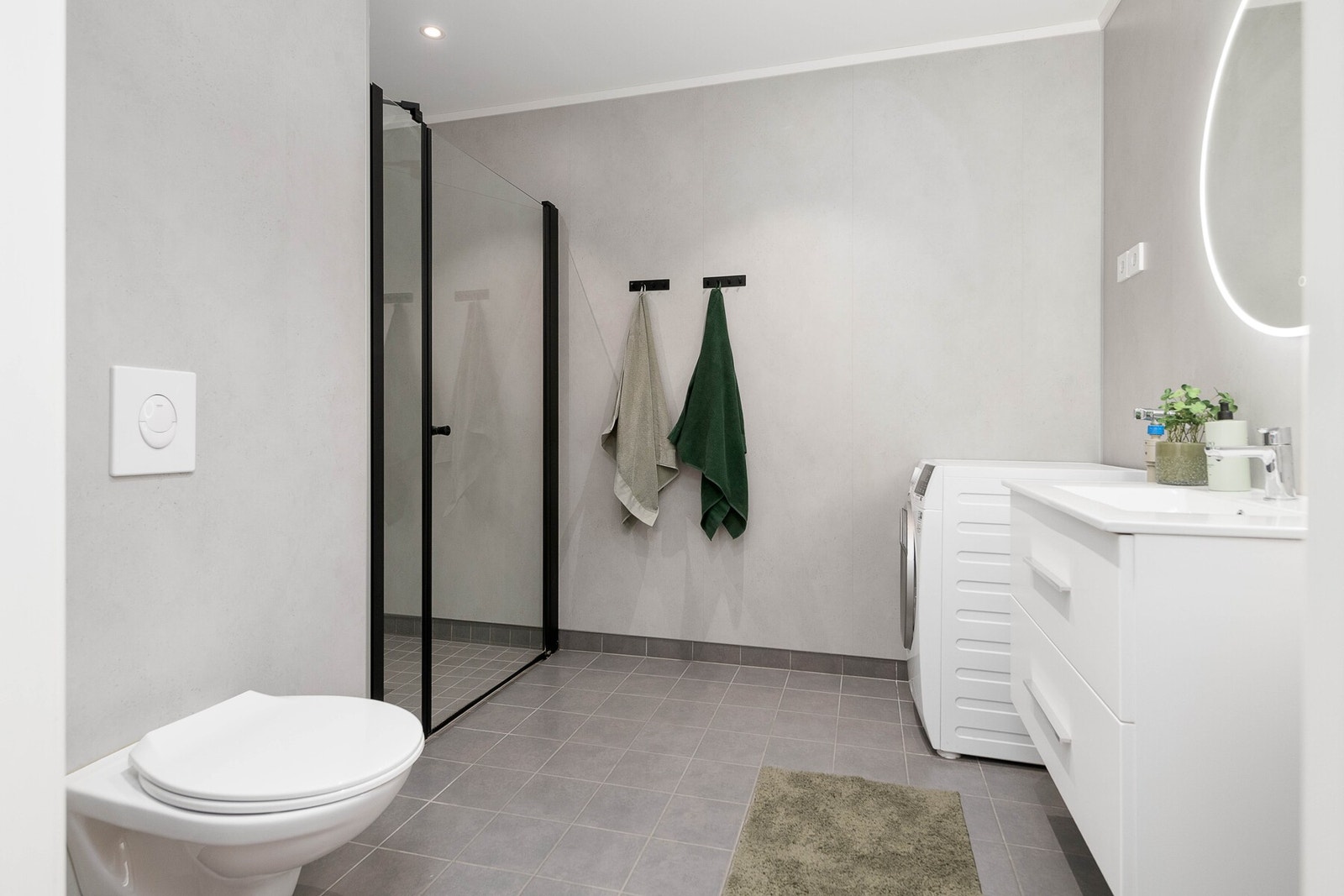 Badet er smakfullt utført med tidsriktige overflater, fargevalg og materialer. Badet har servant på innredning, speil med lys, vegghengt toalett, dusj og opplegg for vaskemaskin. Galleribilde