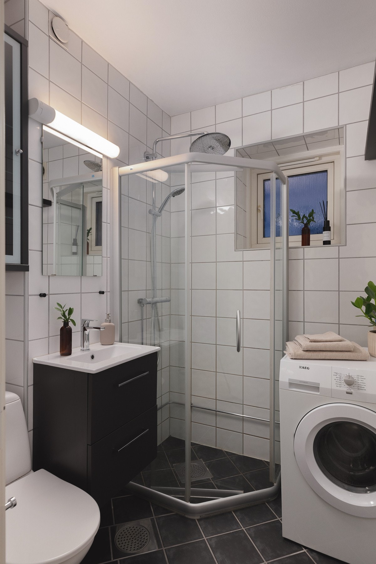 Flislagt baderom med gulvvarme. Badet er innredet med dusjhjørne, toalett, servantskap, speil og opplegg for vaskemaskin. Galleribilde