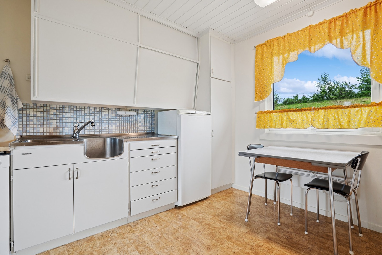 Laminert benkeplate og benkeplate i rustfritt stål med integrert utslagsvask og ettgreps armatur. Flis på vegg over kjøkkenbenk. Galleribilde
