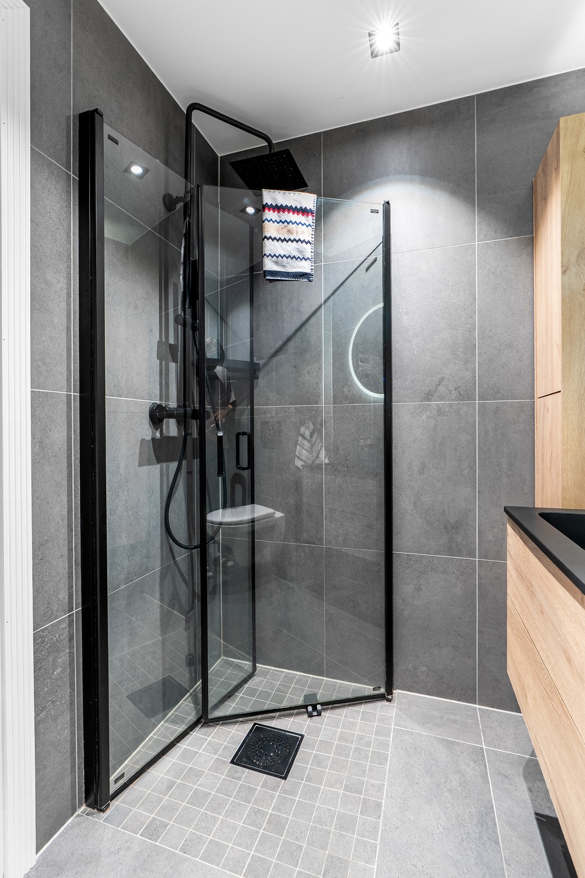 Badet er både moderne og pent, med store fliser og himling med downlights. I hjørnet er det innredet med dusjsone adskilt med to innfellbare glassdører. Galleribilde