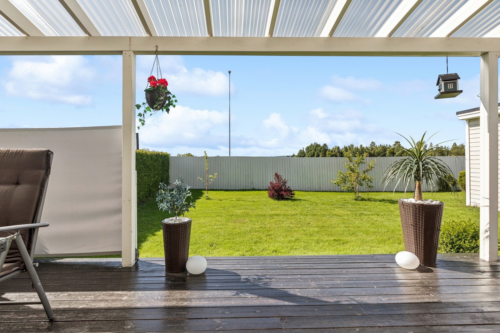 Overbygget terrasse med utsyn til flat og solrik hage - et perfekt sted for avslapning og hyggelige sommerdager. Galleribilde