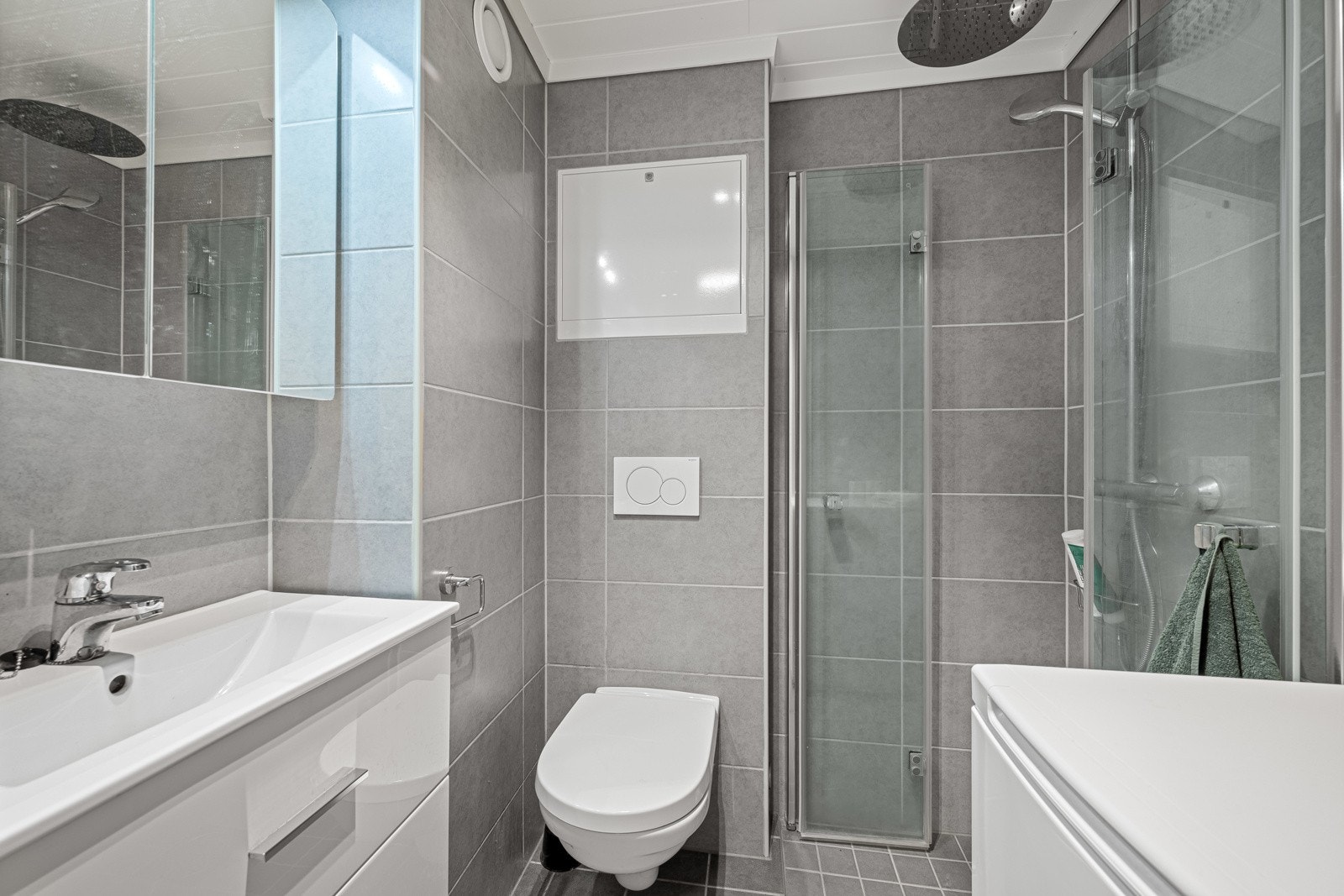Pent flislagt bad som er rehabilitert i regi av borettslaget i 2019. Badet har nedsenket dusjsone med praktiske glassvegger, veggmontert toalett, vask med skuffer og opplegg for vaskemaskin Galleribilde