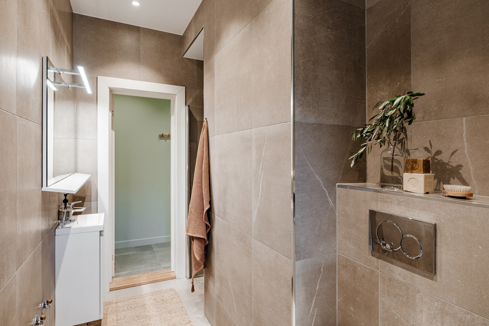 Ellers er badet innredet med vegghengt toalett og smal servant med skap under og vegghengt speil med hylle og belysning over Galleribilde