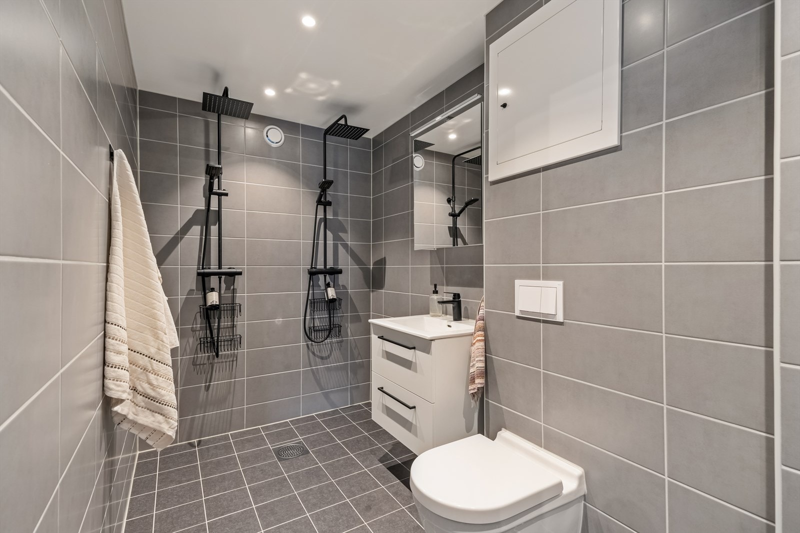 Badet er utstyrt med elektriske varmekabler i gulv, nedfelt servant, veggmontert toalett og to dusjarmaturer. Galleribilde