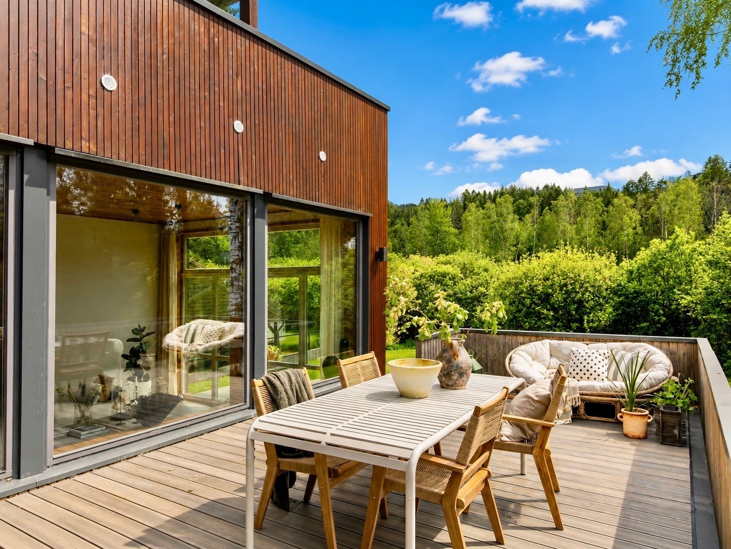 Terrassen utenfor kjøkkenet har en sosial og praktisk beliggenhet, med god kontakt til både stuen og hagen. Boligen er kledd med sibirsk lerk, et eksklusivt og slitesterkt naturmateriale kjent for sin lange levetid. Fargen skyldes behandling med beis. Galleribilde