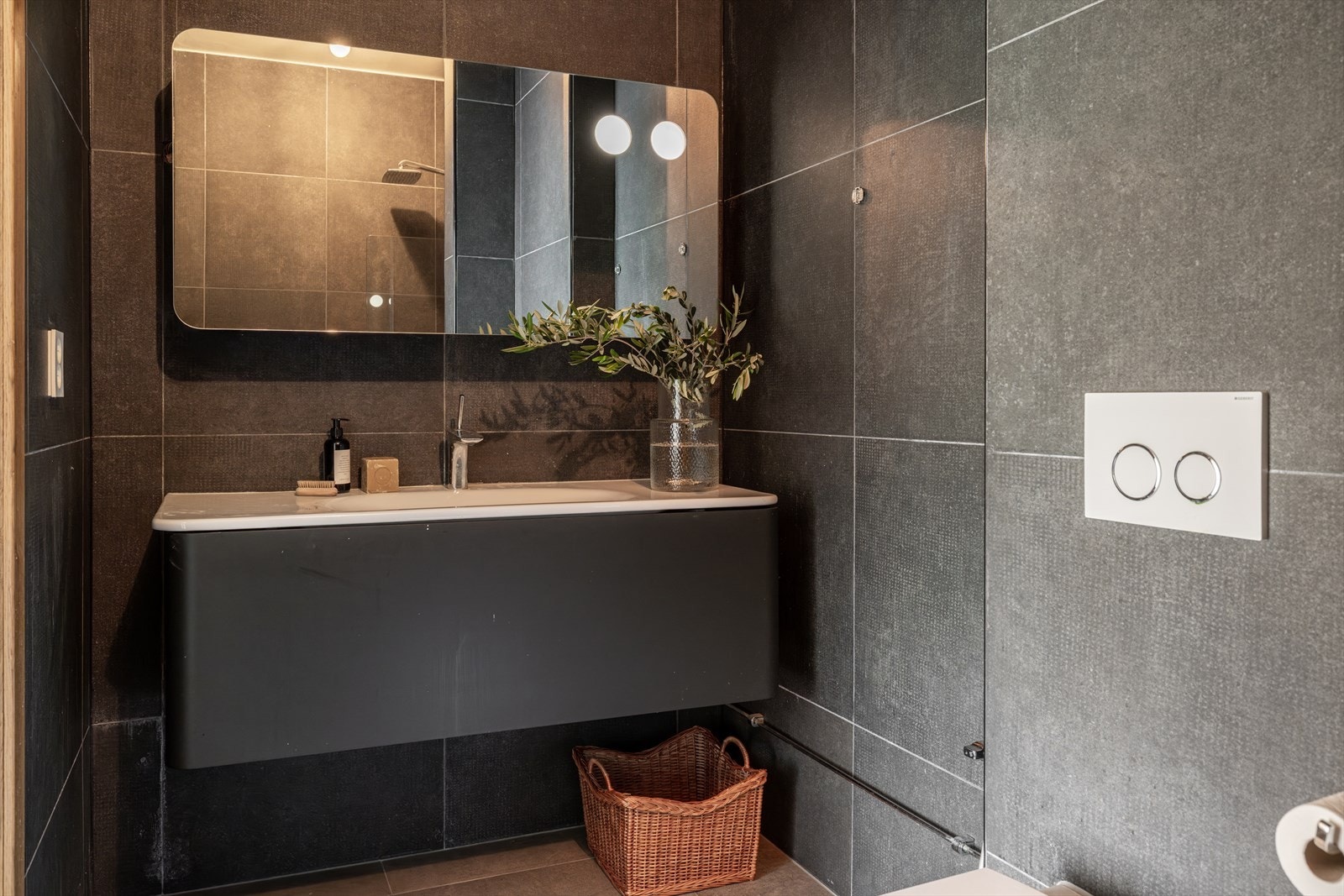 Hovedbadet er inndelt i flere soner og har et gjennomført uttrykk med mørke fargetoner. Material- og fargevalgene skaper en eksklusiv spa- og hotellfølelse, som gir rommet en rolig og avslappende atmosfære. Galleribilde