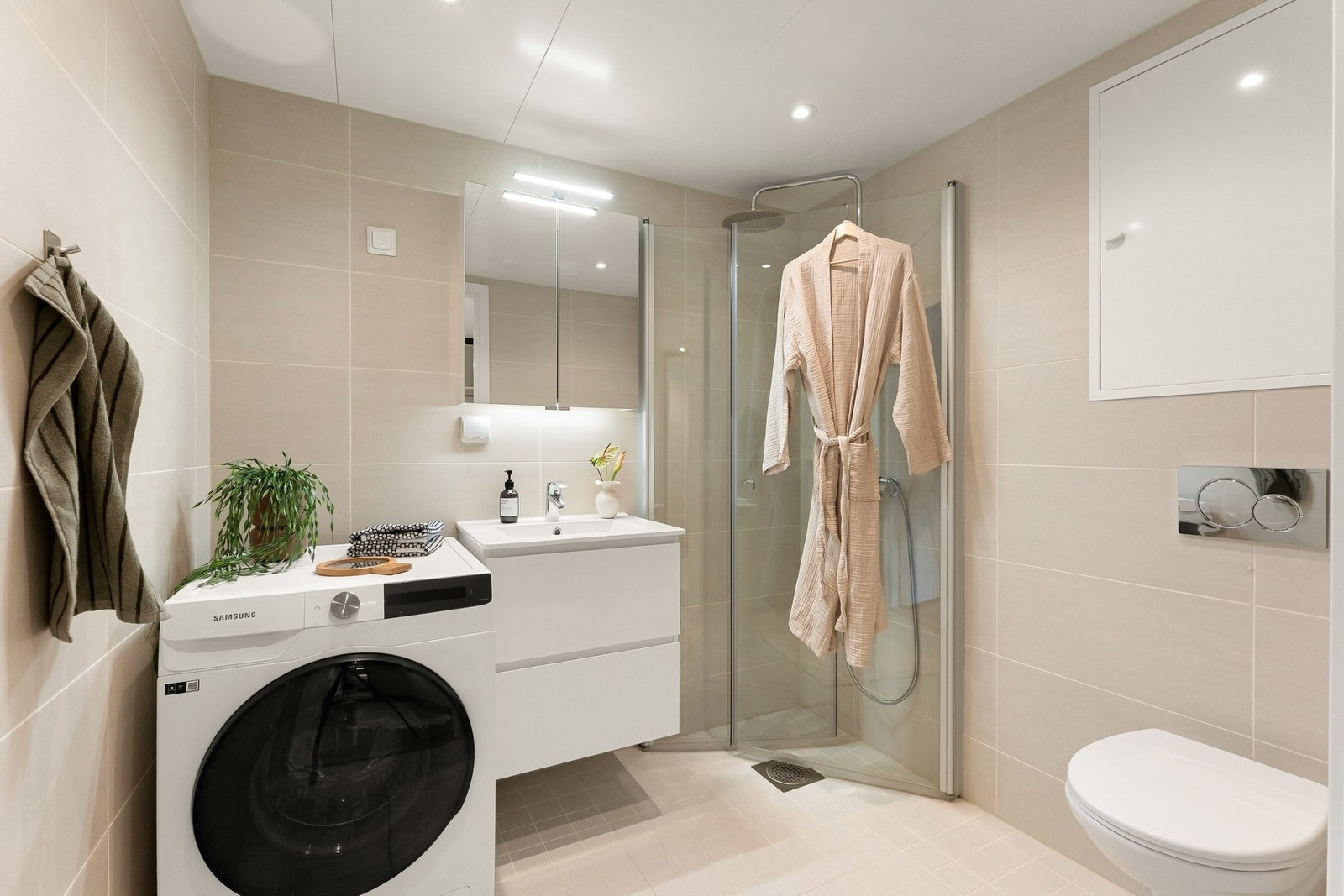 Badet er godt utnyttet og innredet med vegghengt servantskap med glatte fronter og heldekkende servant, speilskap med belysning, vegghengt toalett og en romslig dusjsone med nedsenket gulv og glassdører. Galleribilde