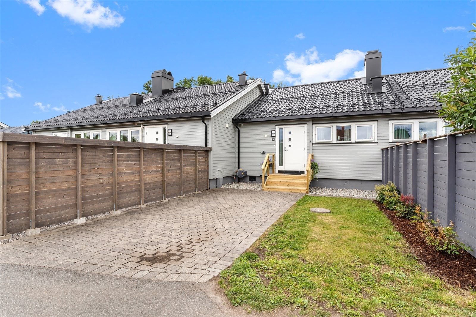 Steinbelagt biloppstillingsplass ved inngangen. Elbil-lader er montert på husveggen. Galleribilde