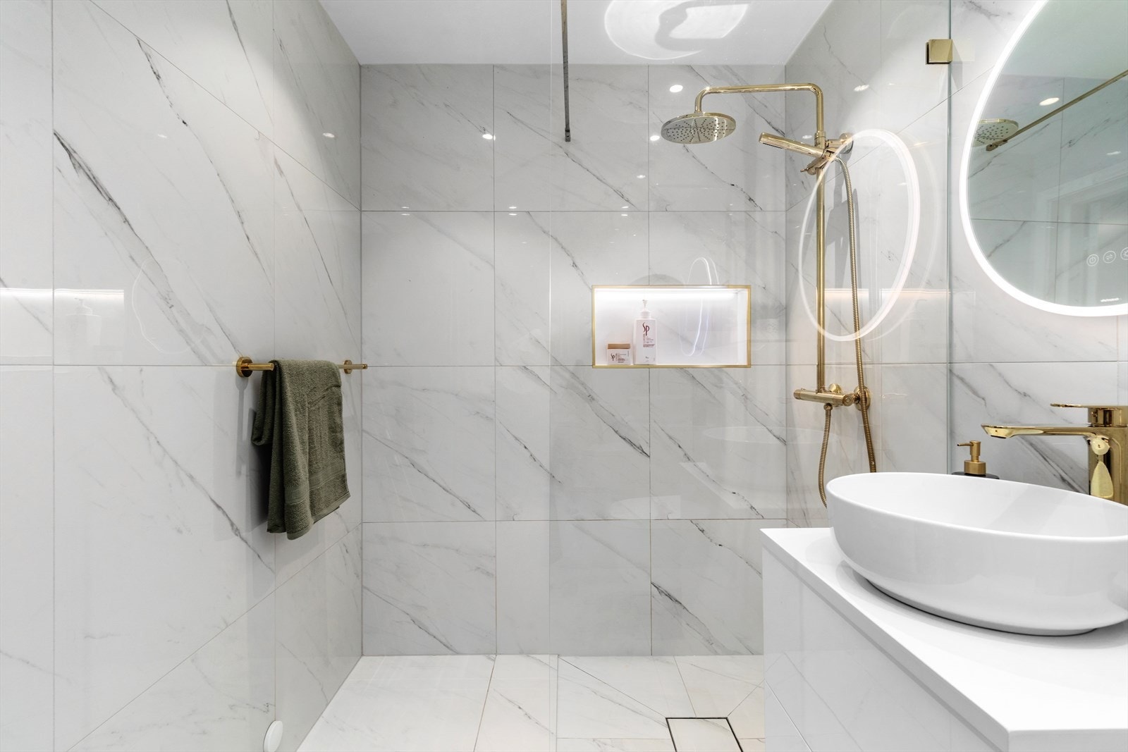 Badet har store fliser på gulvet med underliggende varme, matchende veggfliser og downlightsbelysning i taket. Galleribilde