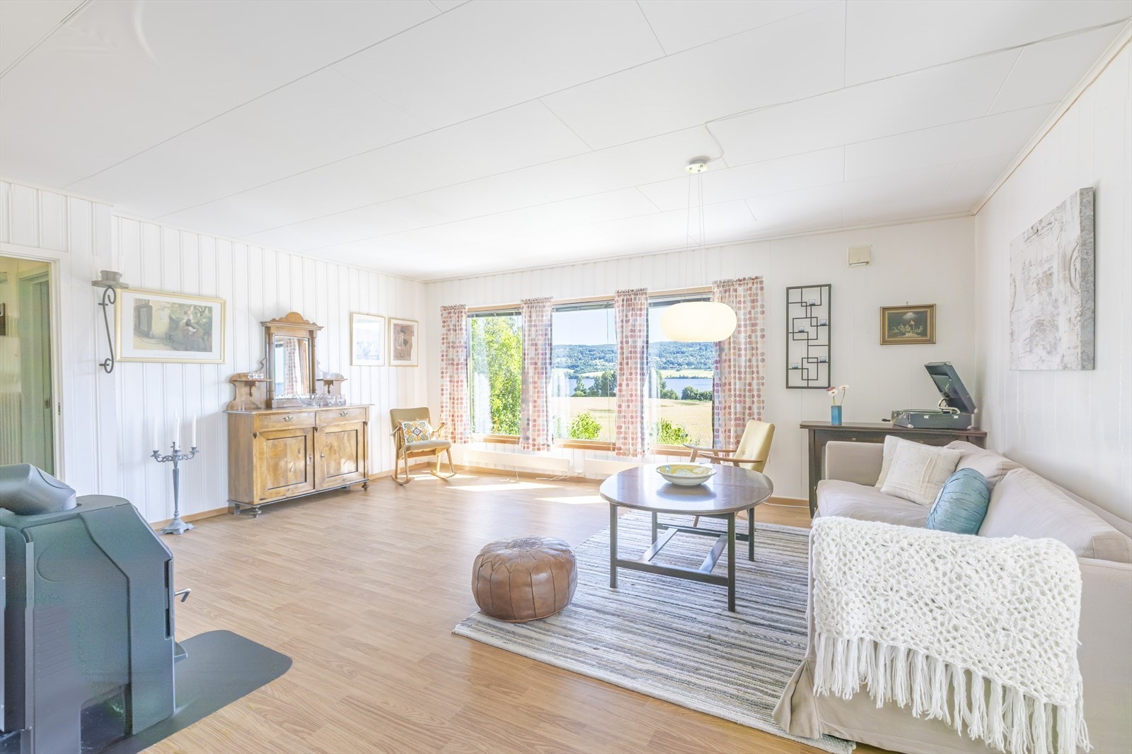 Lys og trivelig stue med peisovn og store vindusflater som slipper inn rikelig med naturlig lys og byr på flott utsikt over åkrene og ned mot fjorden. Foto: GMP Galleribilde