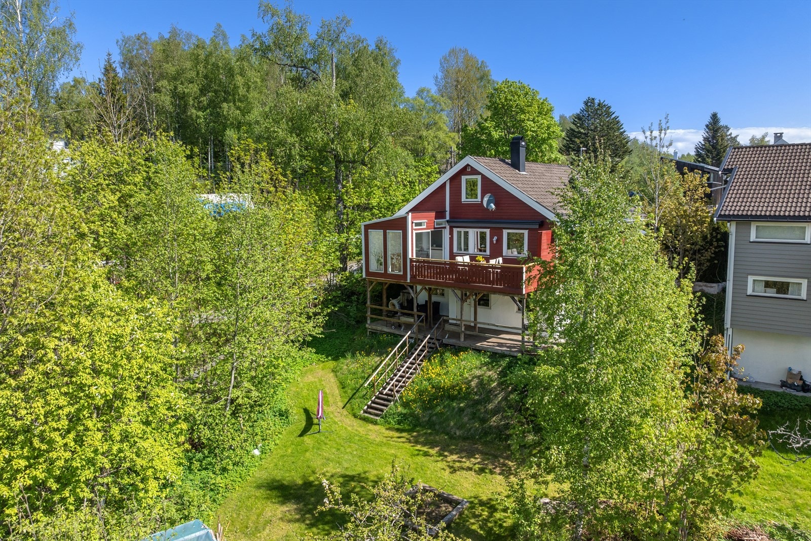 På nedsiden av eiendommen skråner tomten ned mot et grønt og frodig område med gressplen og naturlig vegetasjon, noe som gir en lun og privat ramme rundt eiendommen. Galleribilde